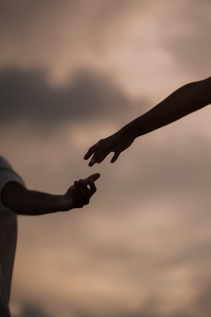 Silhouette of two hands reaching towards each other at sunset, symbolizing connection and hope.