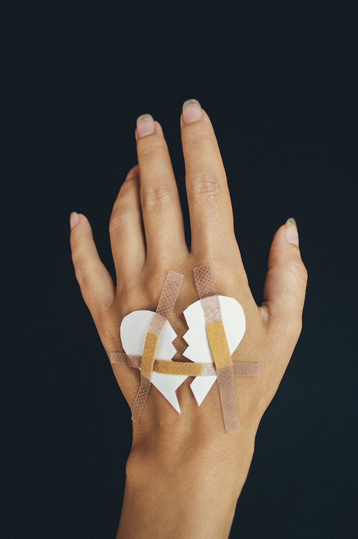 services-07 A hand with a paper broken heart mended by band-aids on a dark background.