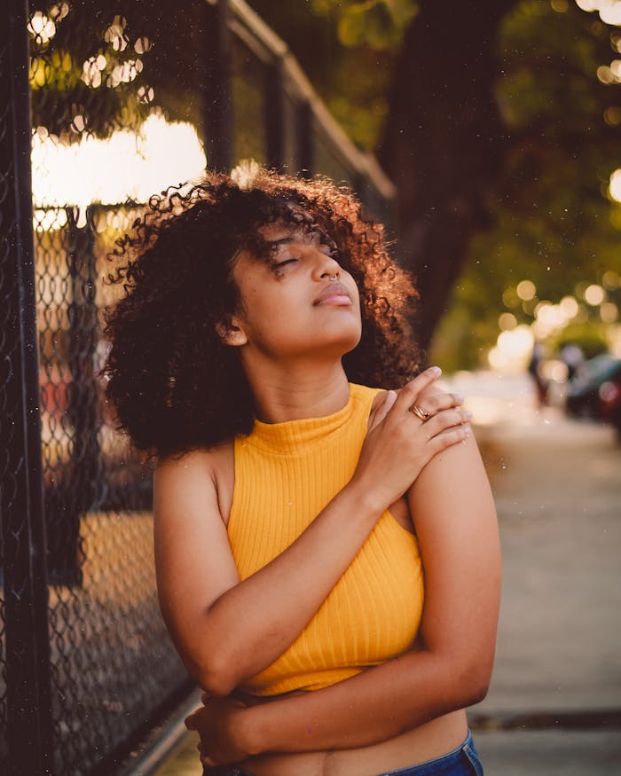 Young woman with curly hair enjoying a sunny day outdoors, exuding confidence.