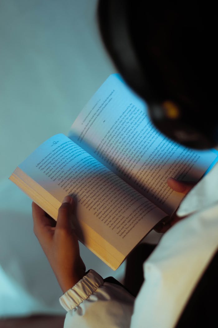 Close-up of a person reading a book while listening through headphones, suggesting focus and learning.
