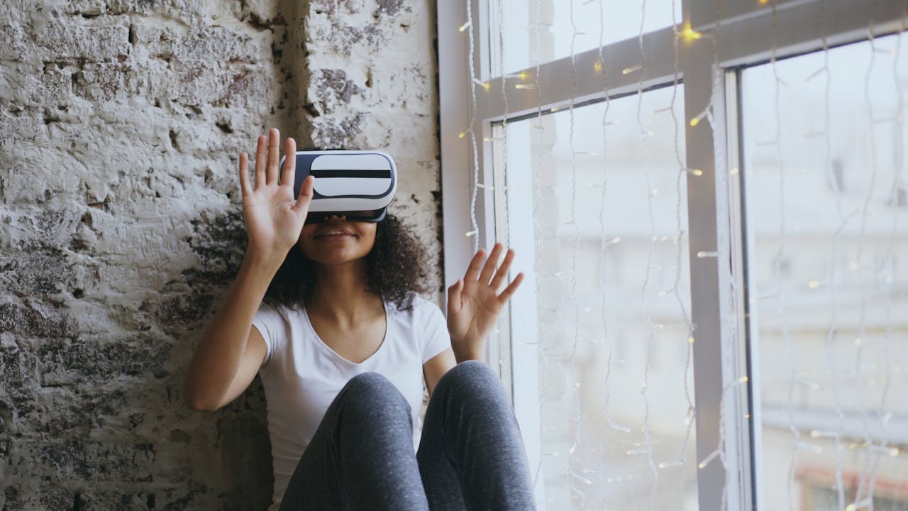 Smiling woman using VR headset by a window, experiencing virtual reality at home.